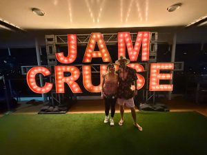An image of Rachel and Sasha standing in front of the illuminated Jam Cruise sign on the boat inside the magic of jam cruise