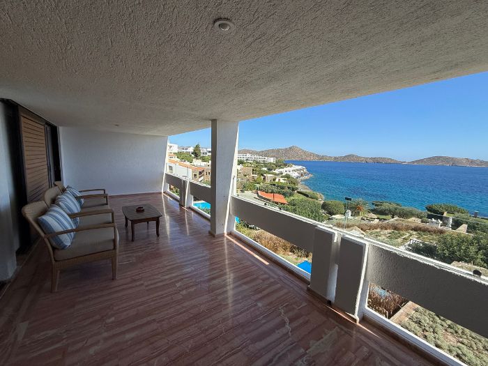 Spacious covered balcony with outdoor seating overlooking the blue waters of Mirabello Bay at Elounda Mare in Crete.