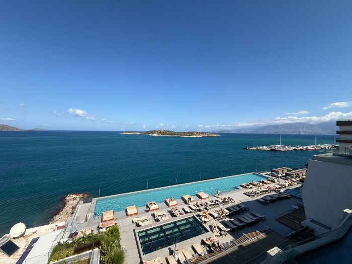 Rooftop infinity pool with lounge chairs overlooking the blue sea and coastline at InterContinental Crete in Agios Nikolaos.