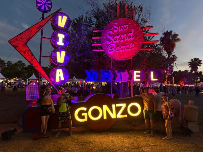 Friends posing in front of the colorful, illuminated Viva El Gonzo festival sign at night in Cabo San Lucas, Mexico.